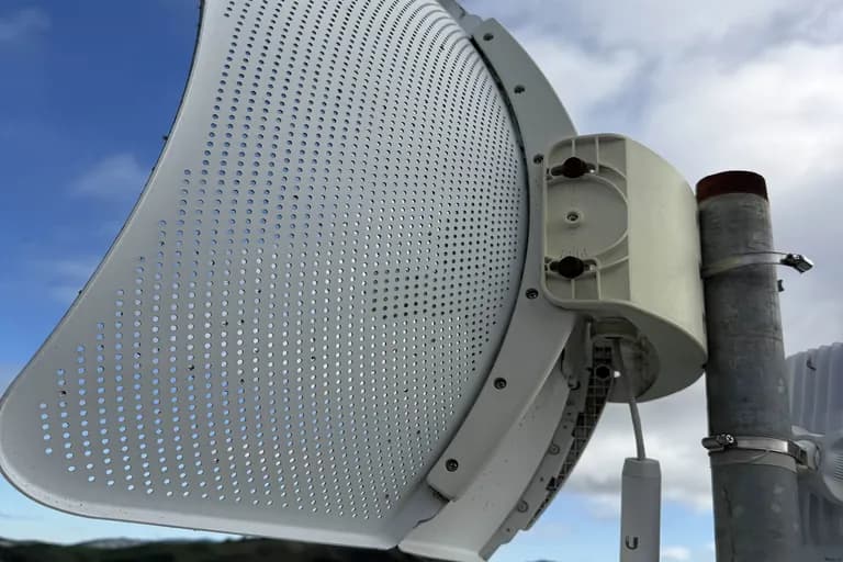 Low-angle view of a perforated parabolic dish against blue sky with cumulus, off-grid Sonoma hilltop install.